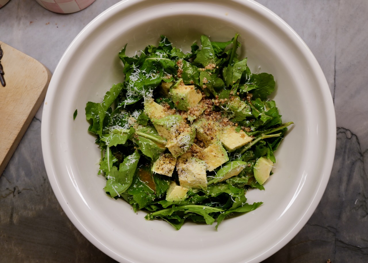 wild arugula salad with avocado in white salad bowl